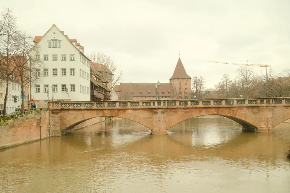 Malersicher Blick auf eine historische Brücke in Nürnberg über einen ruhigen Fluss bei bewölktem Himmel.